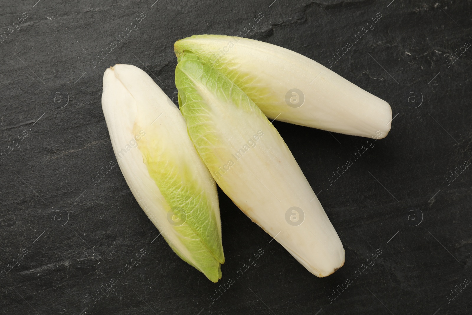 Photo of Fresh raw Belgian endives (chicory) on black table, top view