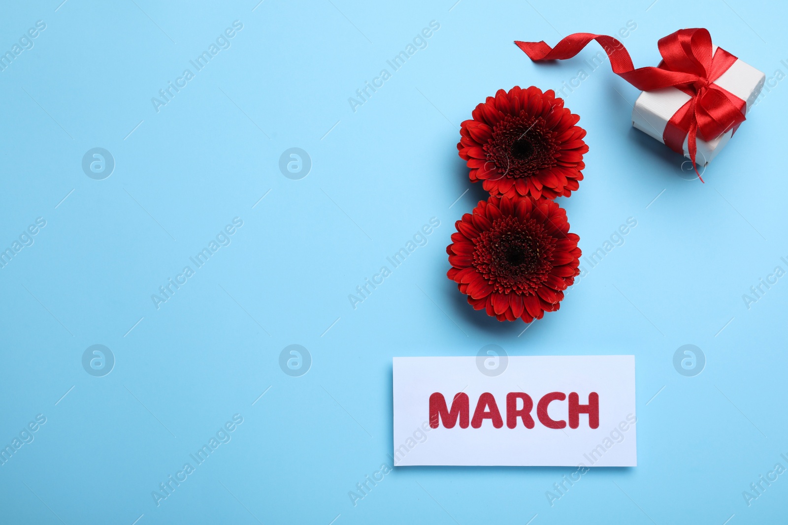 Photo of 8 March greeting card design with red gerberas, gift box and space for text on light blue background, flat lay. International Women's day