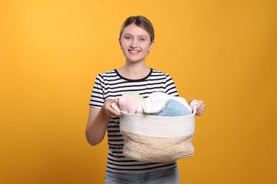 Happy woman with basket full of laundry on orange background