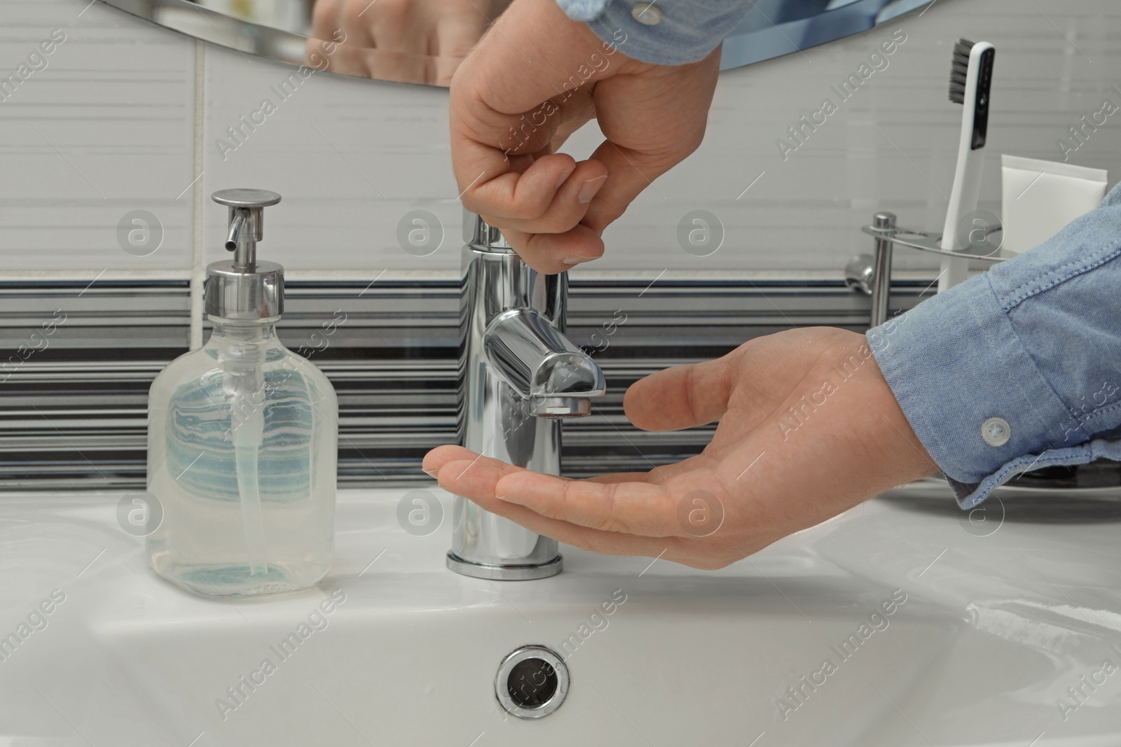 Photo of Man using water tap to wash hands in bathroom, closeup