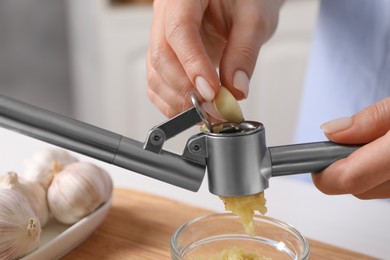 Photo of Woman squeezing garlic with press at wooden table indoors, closeup