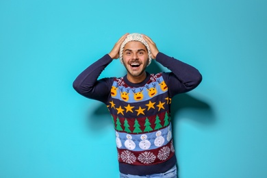 Young man in Christmas sweater and knitted hat on color background