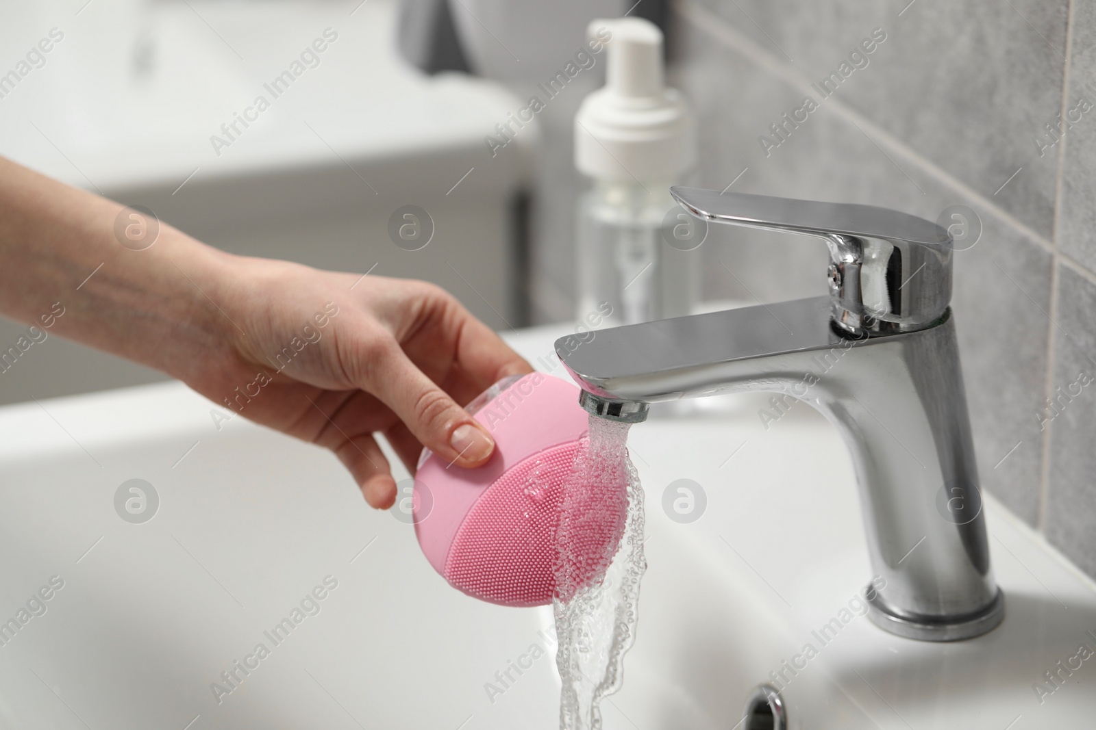 Photo of Young woman washing facial brush in bathroom, closeup