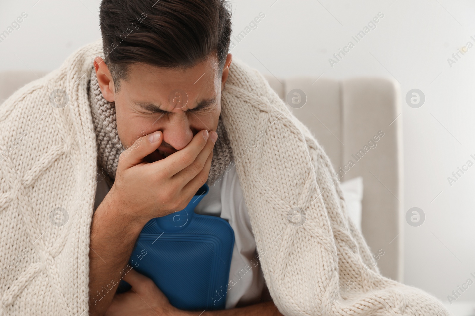 Photo of Ill man with hot water bottle coughing at home