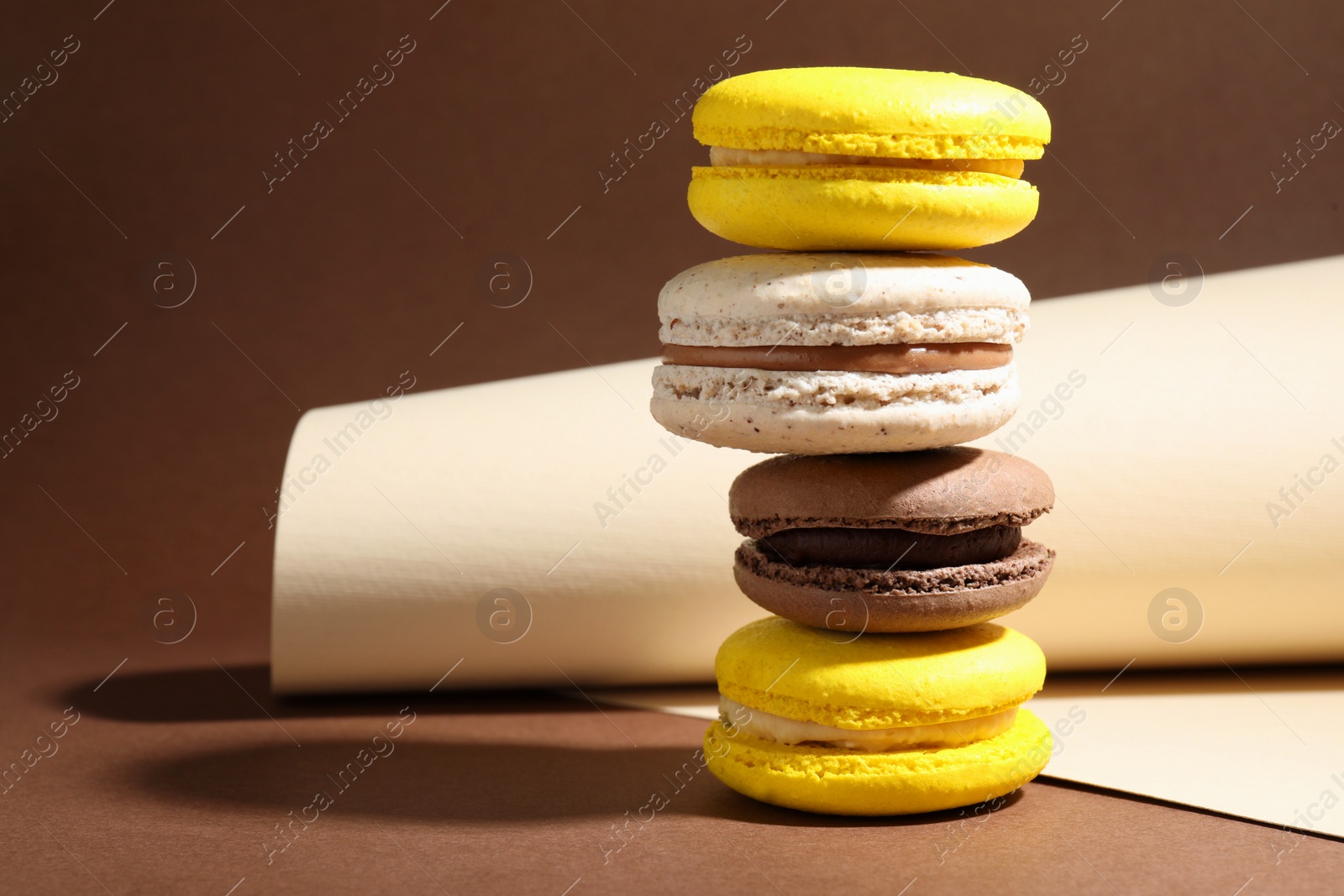 Photo of Stack of colorful macarons and paper roll on brown background. Space for text