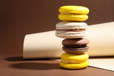 Stack of colorful macarons and paper roll on brown background. Space for text
