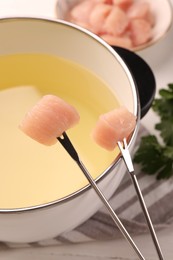 Photo of Fondue pot with oil, forks, raw meat pieces and parsley on white wooden table, closeup