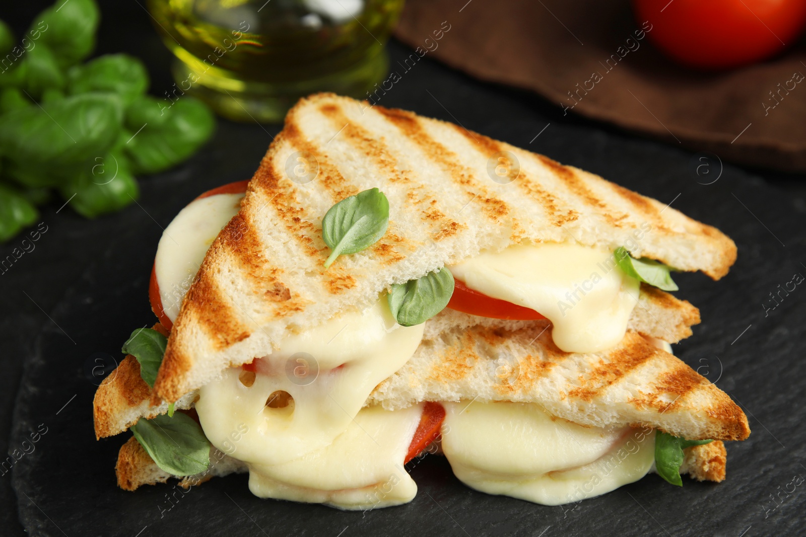 Photo of Delicious grilled sandwiches with mozzarella, tomatoes and basil on black board