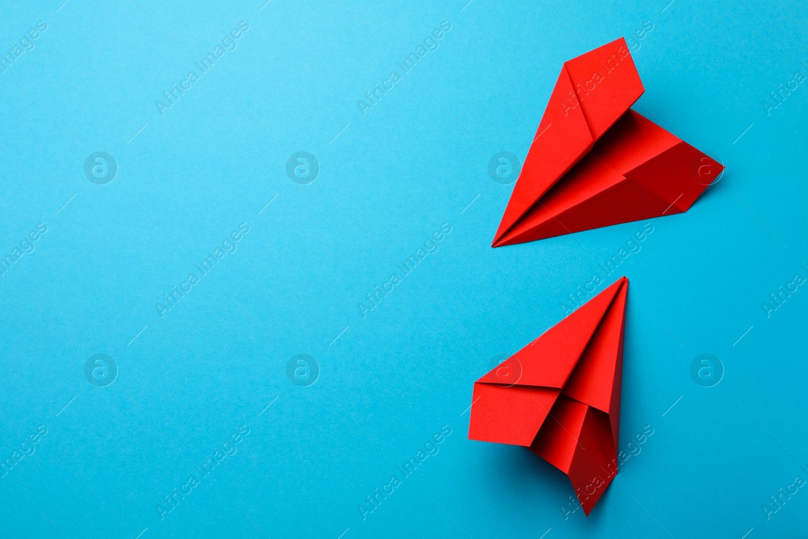 Photo of Handmade red paper planes on light blue background, flat lay. Space for text