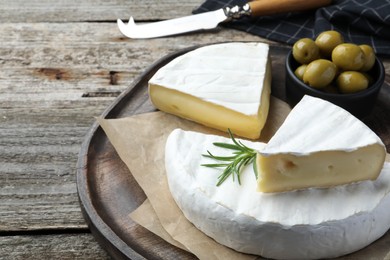 Photo of Tasty cut brie cheese with rosemary and olives on wooden table