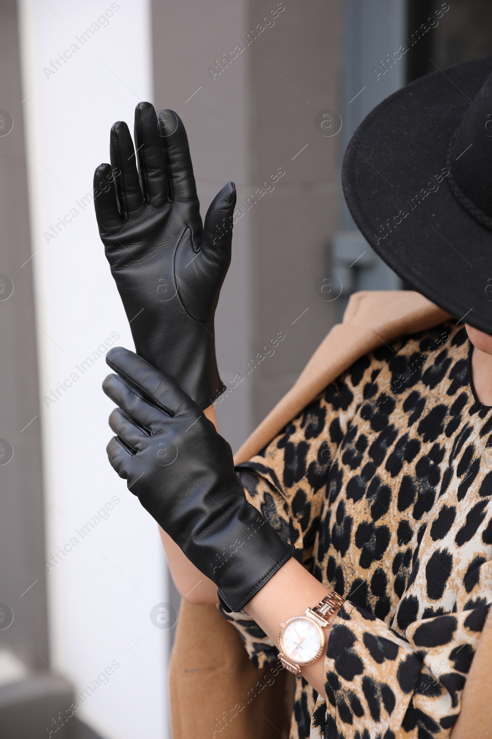 Photo of Young woman putting on stylish black leather gloves outdoors, closeup