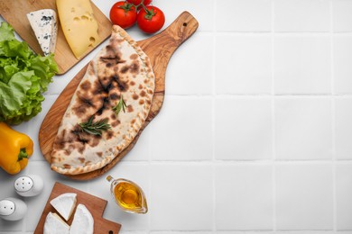 Photo of Tasty pizza calzone with cheese and different products on white tiled table, flat lay. Space for text