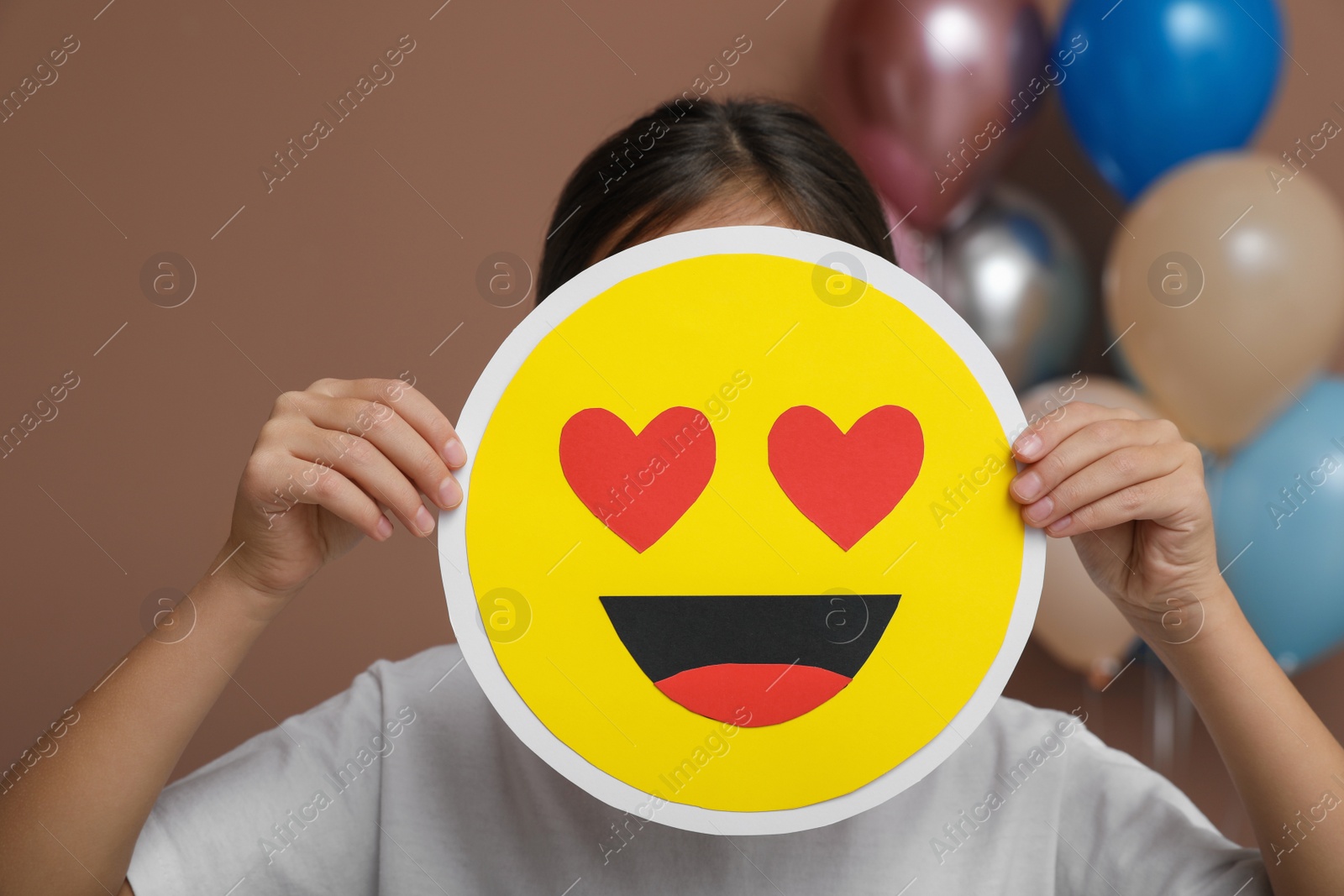 Photo of Little girl covering face with heart eyes emoji in decorated room