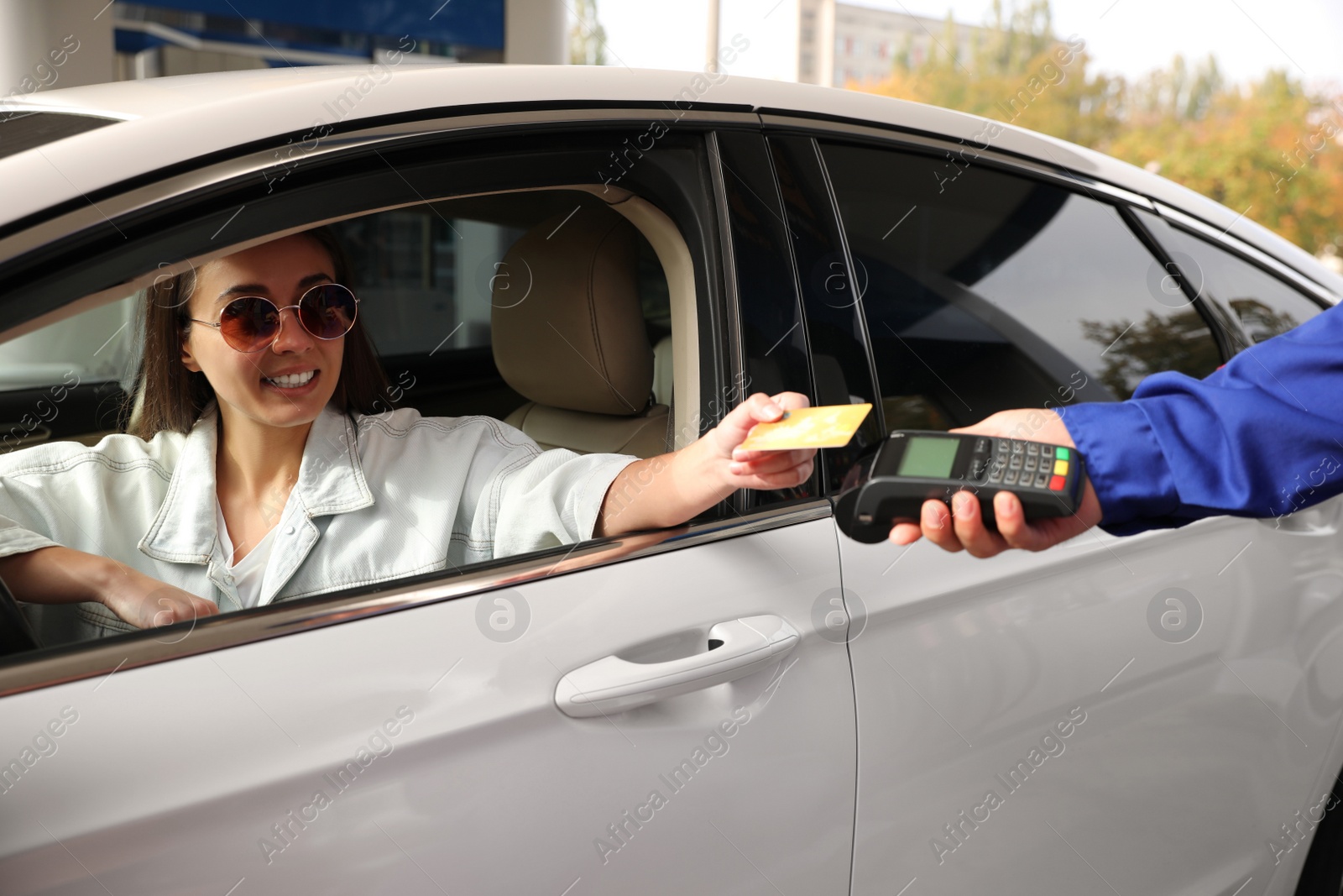 Photo of Woman sitting in car and paying with credit card at gas station