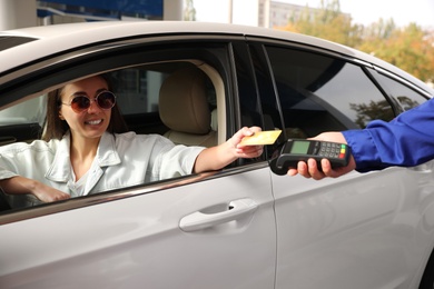 Photo of Woman sitting in car and paying with credit card at gas station