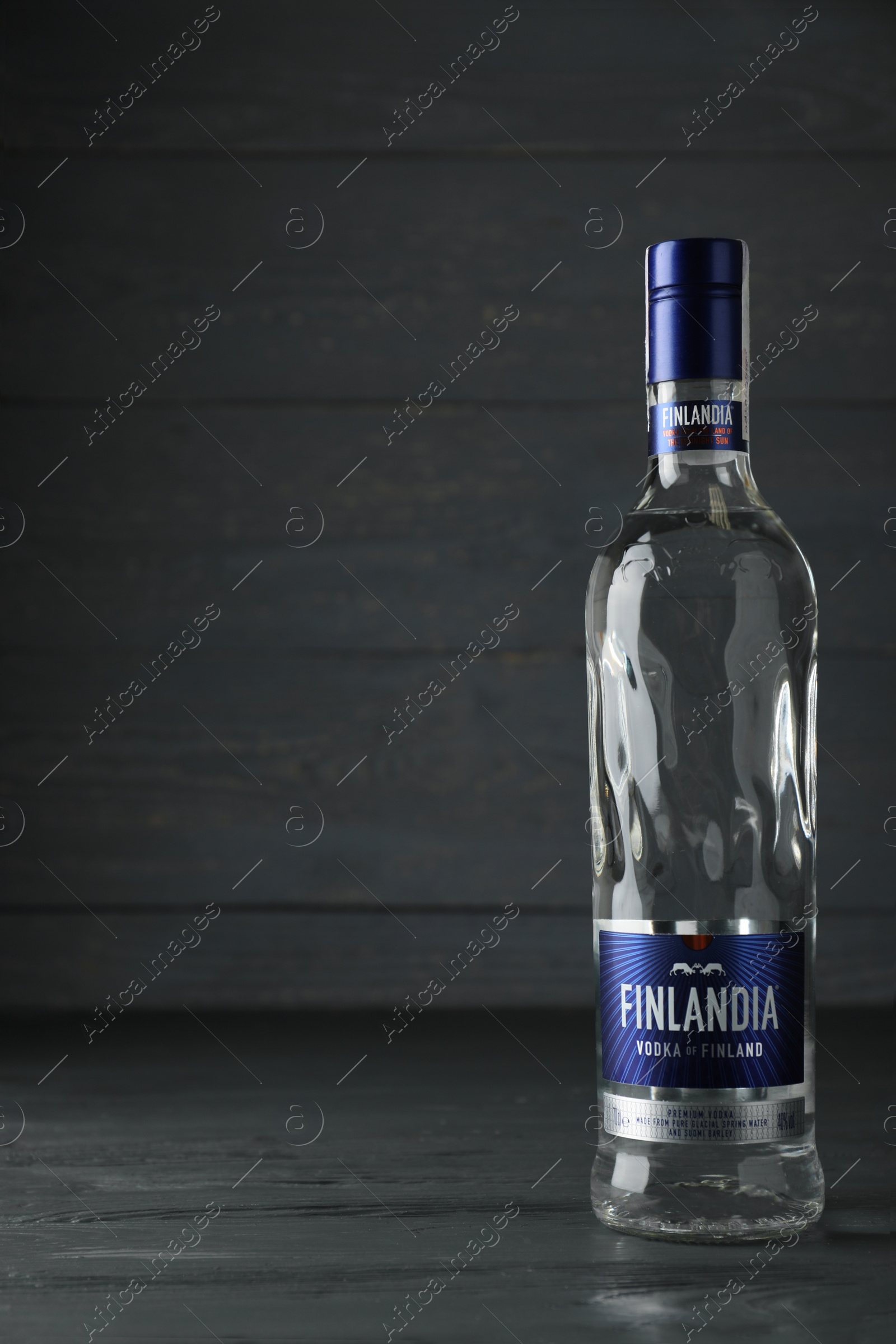 Photo of MYKOLAIV, UKRAINE - OCTOBER 03, 2019: Bottle of Finlandia vodka on wooden table against grey background. Space for text