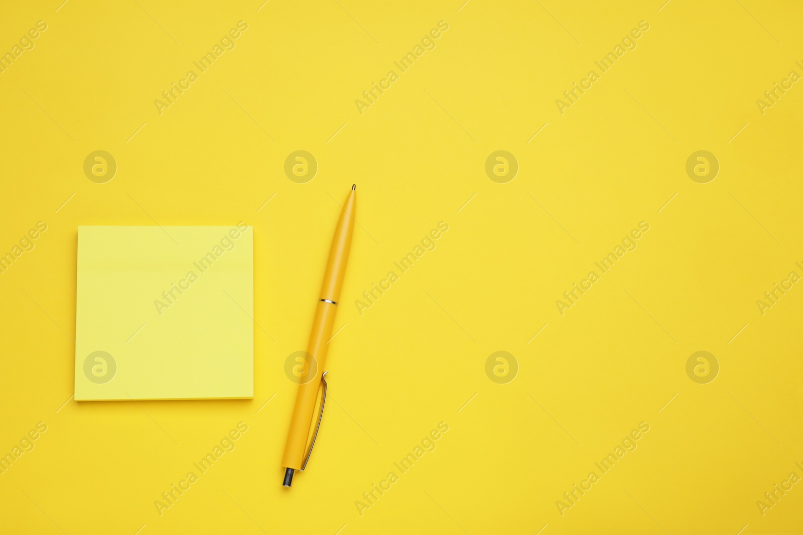 Photo of Paper note and pen on yellow background, flat lay. Space for text