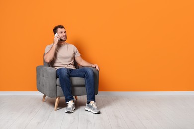 Young man talking on smartphone while sitting in armchair indoors. Space for text