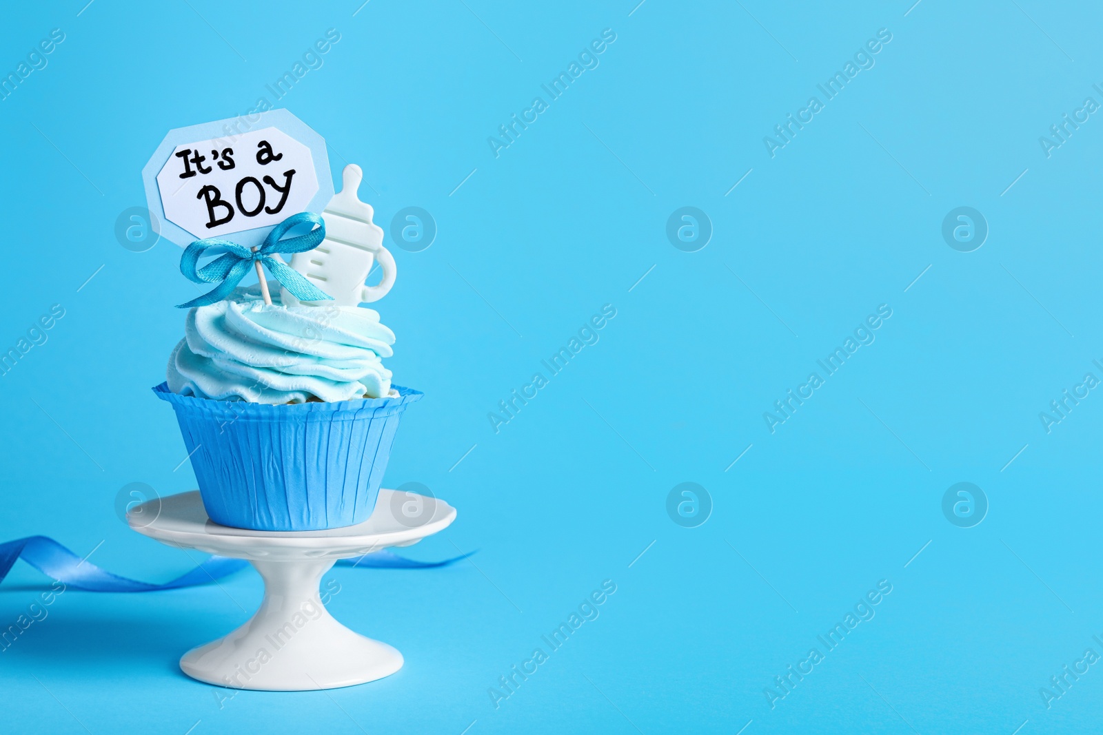 Photo of Beautifully decorated baby shower cupcake with cream and boy topper on light blue background. Space for text