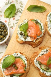 Photo of Tasty canapes with salmon, capers, cucumber and sauce on table, top view