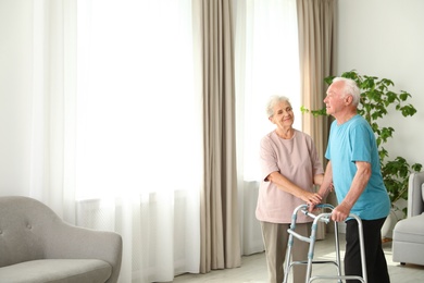 Photo of Elderly woman and her husband with walking frame indoors. Space for text