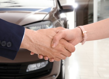 Image of Woman buying car and shaking hands with salesman against blurred auto, closeup