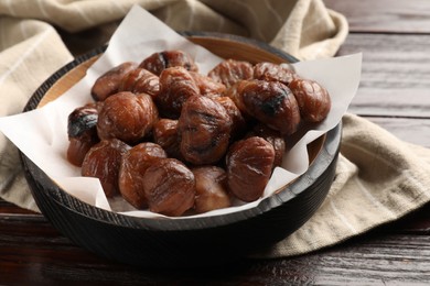 Photo of Roasted edible sweet chestnuts in bowl on wooden table, closeup