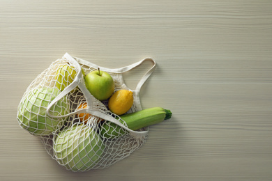 Net bag with vegetables and fruits on wooden table, top view. Space for text