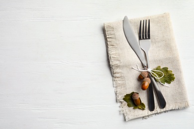 Photo of Cutlery, acorns and dry leaves on white wooden background, flat lay with space for text. Table setting elements