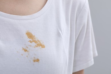 Photo of Woman wearing white t-shirt with stain against light grey background, closeup