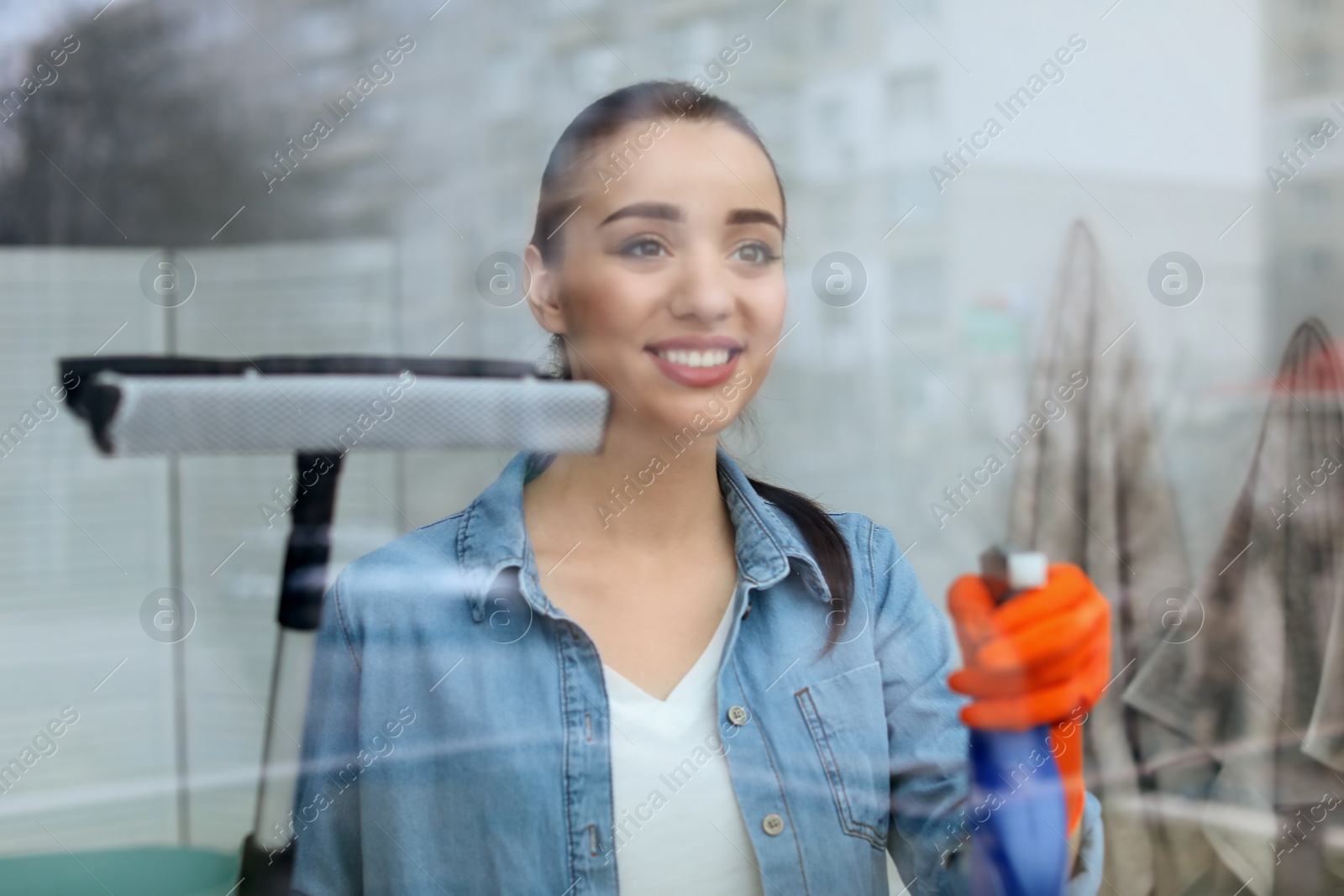 Photo of Young woman cleaning window glass at home