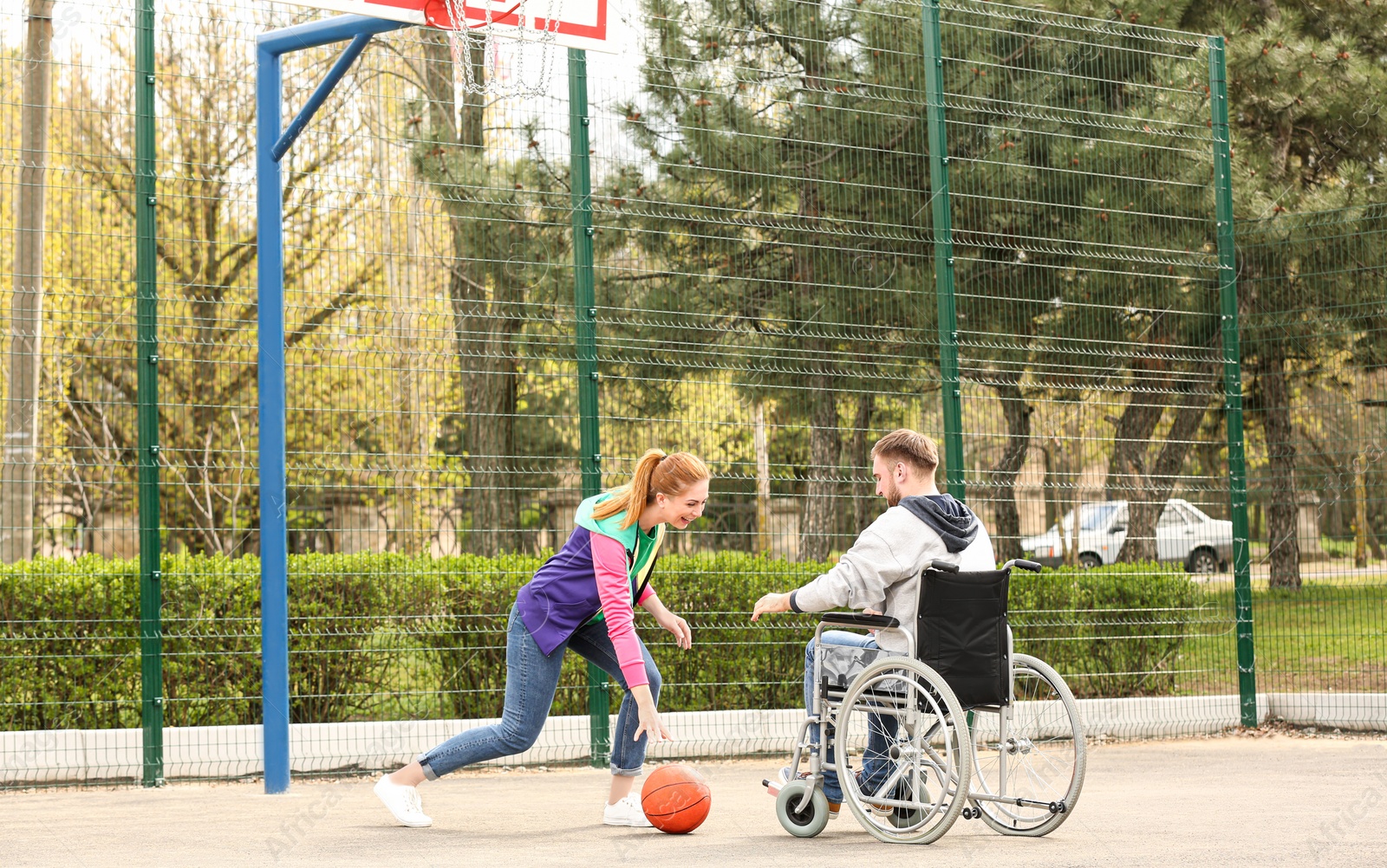 Photo of Man in wheelchair and young woman playing basketball on sports ground