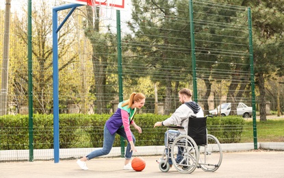 Photo of Man in wheelchair and young woman playing basketball on sports ground