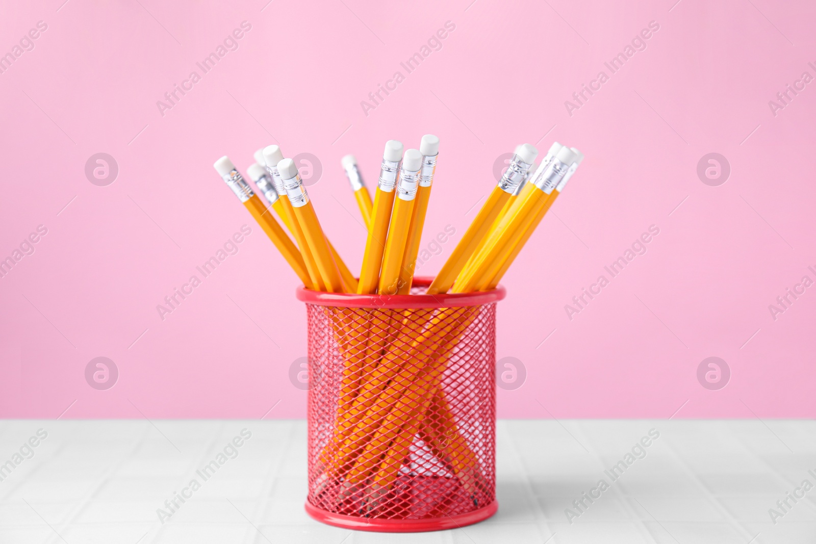 Photo of Many sharp pencils in holder on light table against pink background