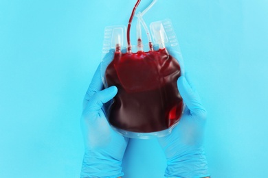 Doctor in gloves holding blood pack on color background, top view. Donation day