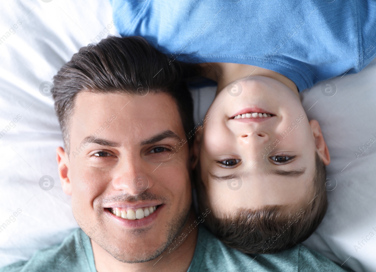 Photo of Happy dad and son on bed, top view. Happy Father's Day