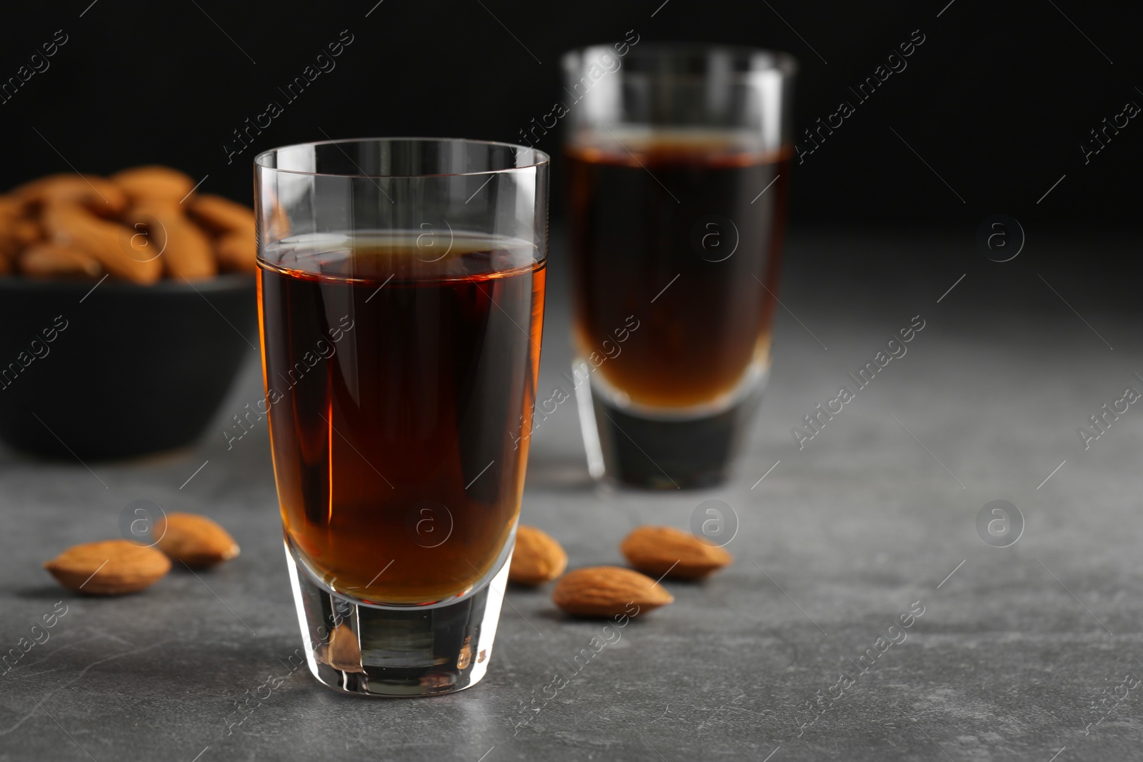 Photo of Glasses with tasty amaretto liqueur and almonds on gray table, closeup. Space for text