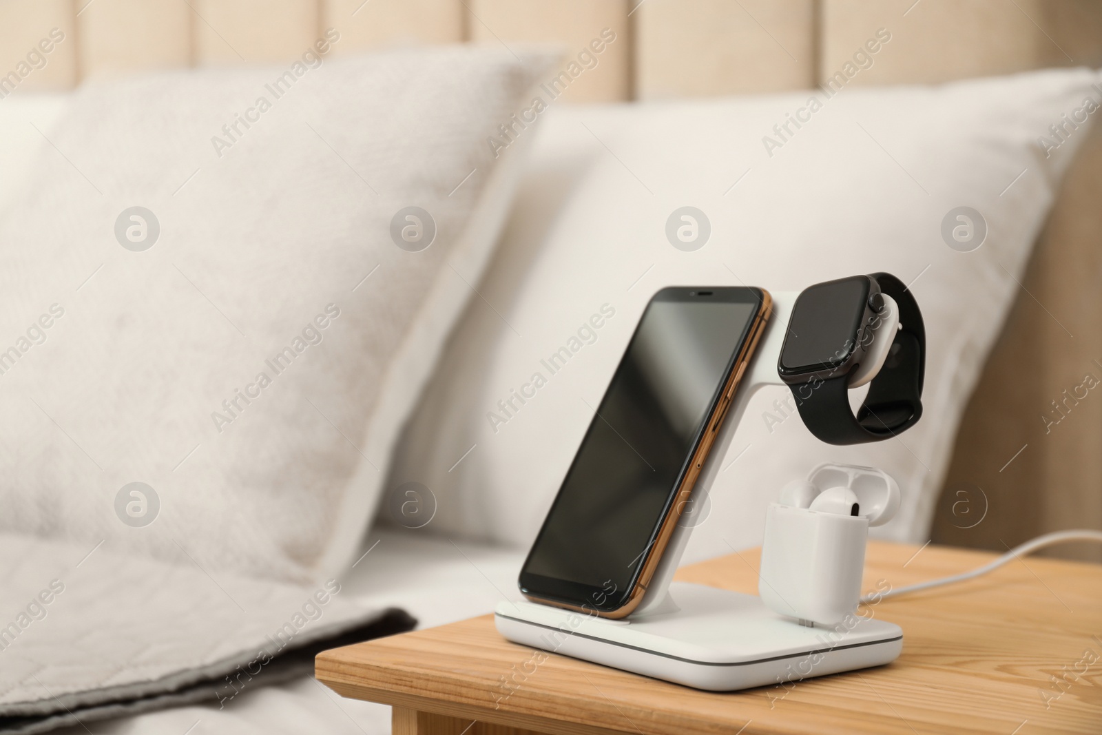 Photo of Different gadgets charging on wireless pad in bedroom. Space for text