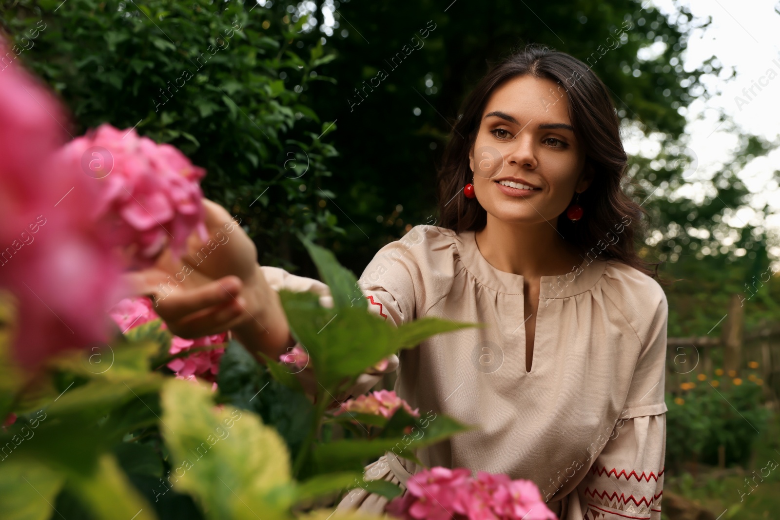 Photo of Beautiful woman wearing embroidered dress in blooming garden. Ukrainian national clothes