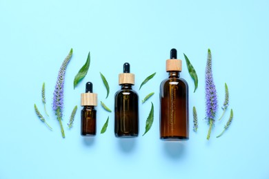 Different bottles of essential oil, flowers and leaves on light blue background, flat lay