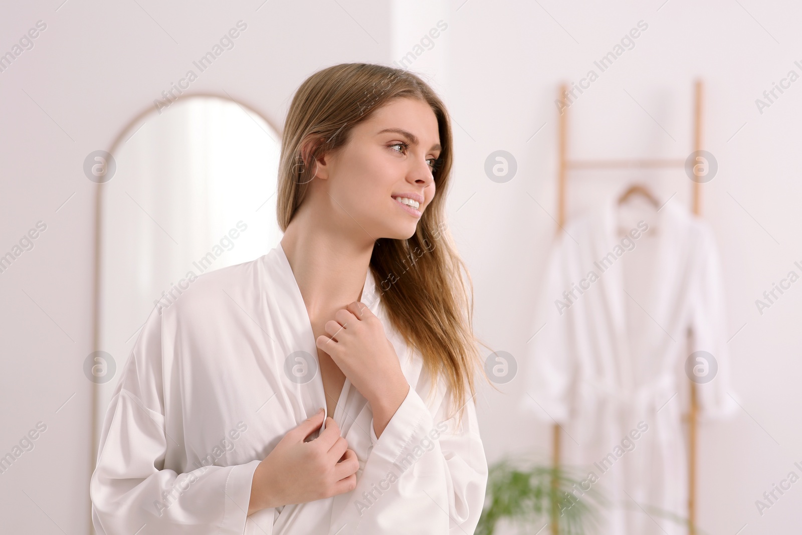 Photo of Beautiful happy woman wearing stylish white robe in bathroom