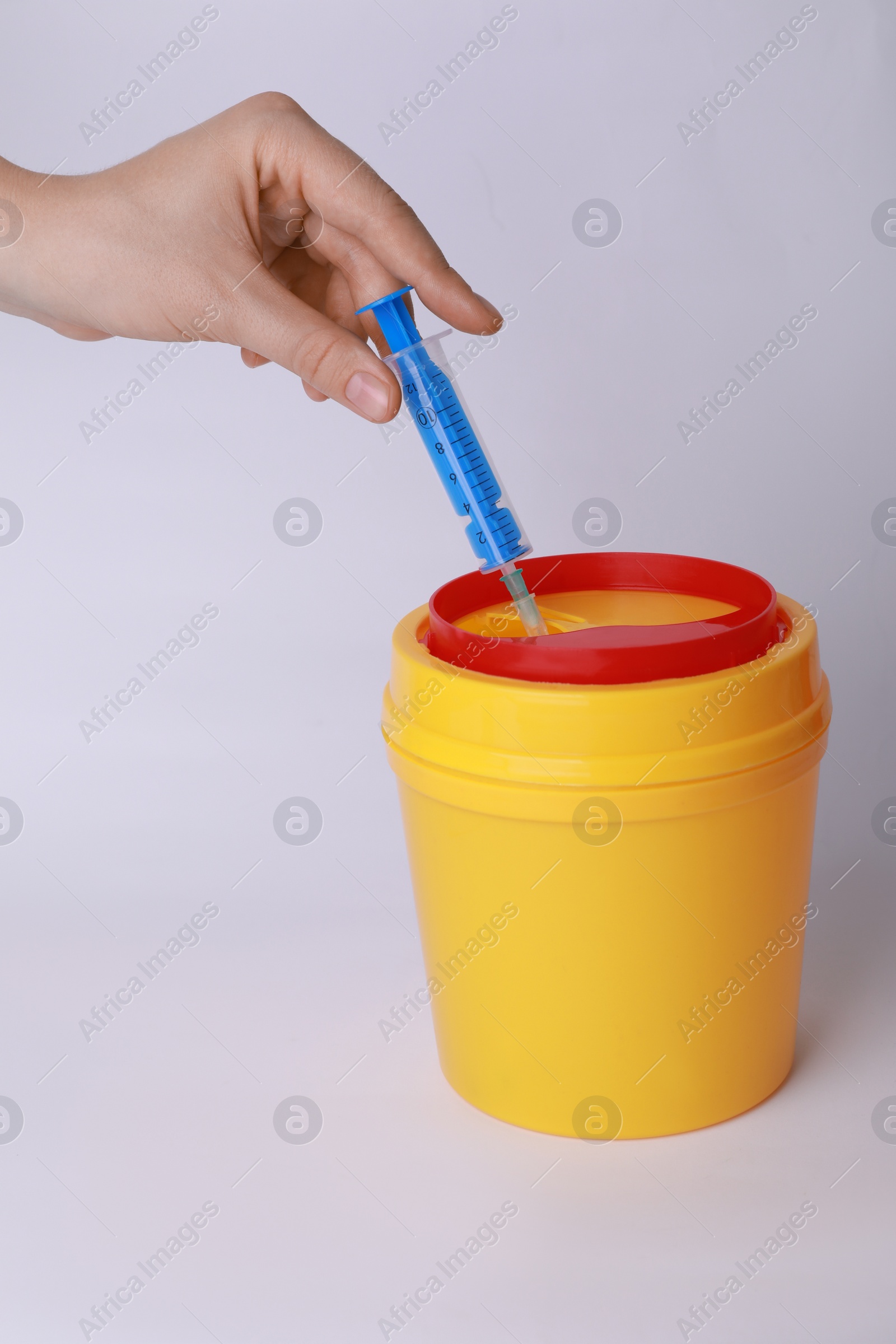 Photo of Woman throwing used syringe into sharps container on white background, closeup