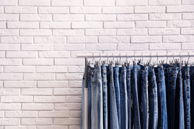 Photo of Rack with stylish jeans near brick wall. Space for text