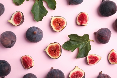 Delicious ripe figs and green leaves on pink background, flat lay