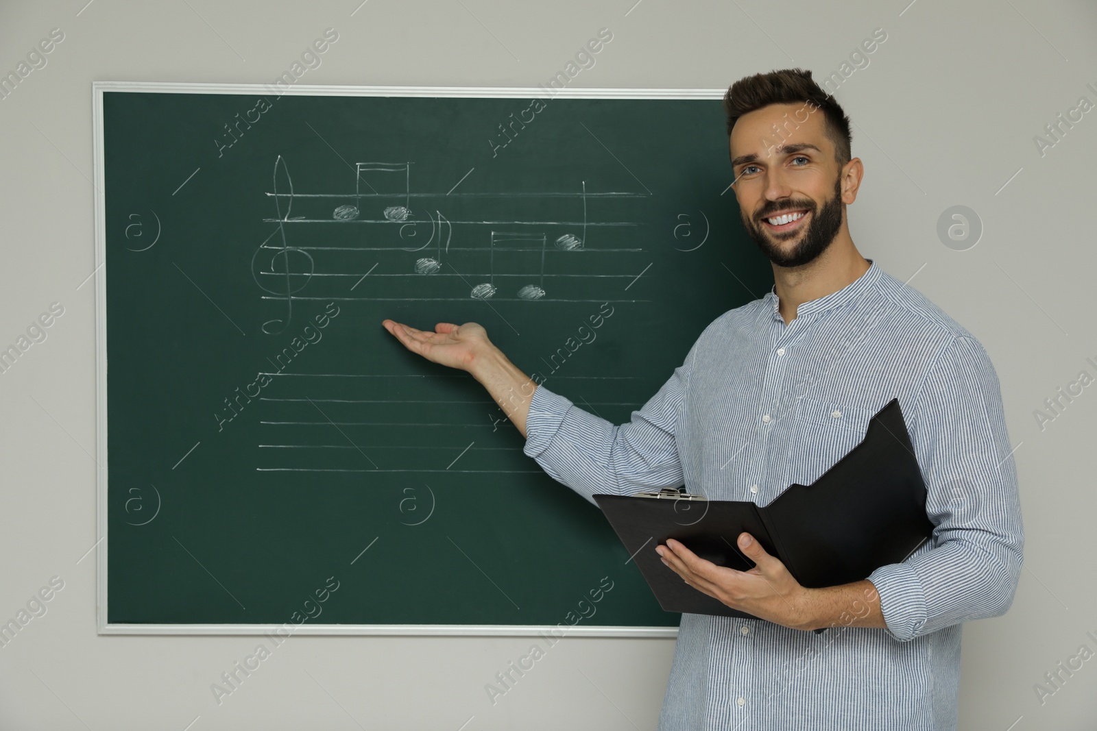 Photo of Teacher near green chalkboard with music notes in classroom