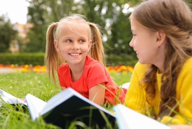 Photo of Cute little girls reading books on green grass in park
