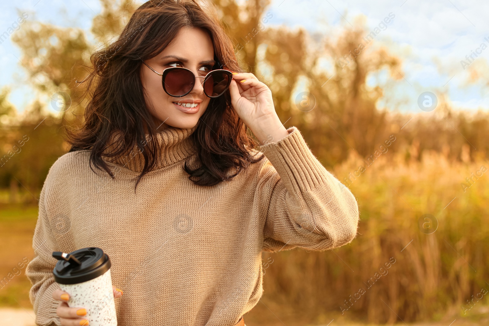 Photo of Beautiful young woman with cup of coffee wearing stylish autumn sweater outdoors