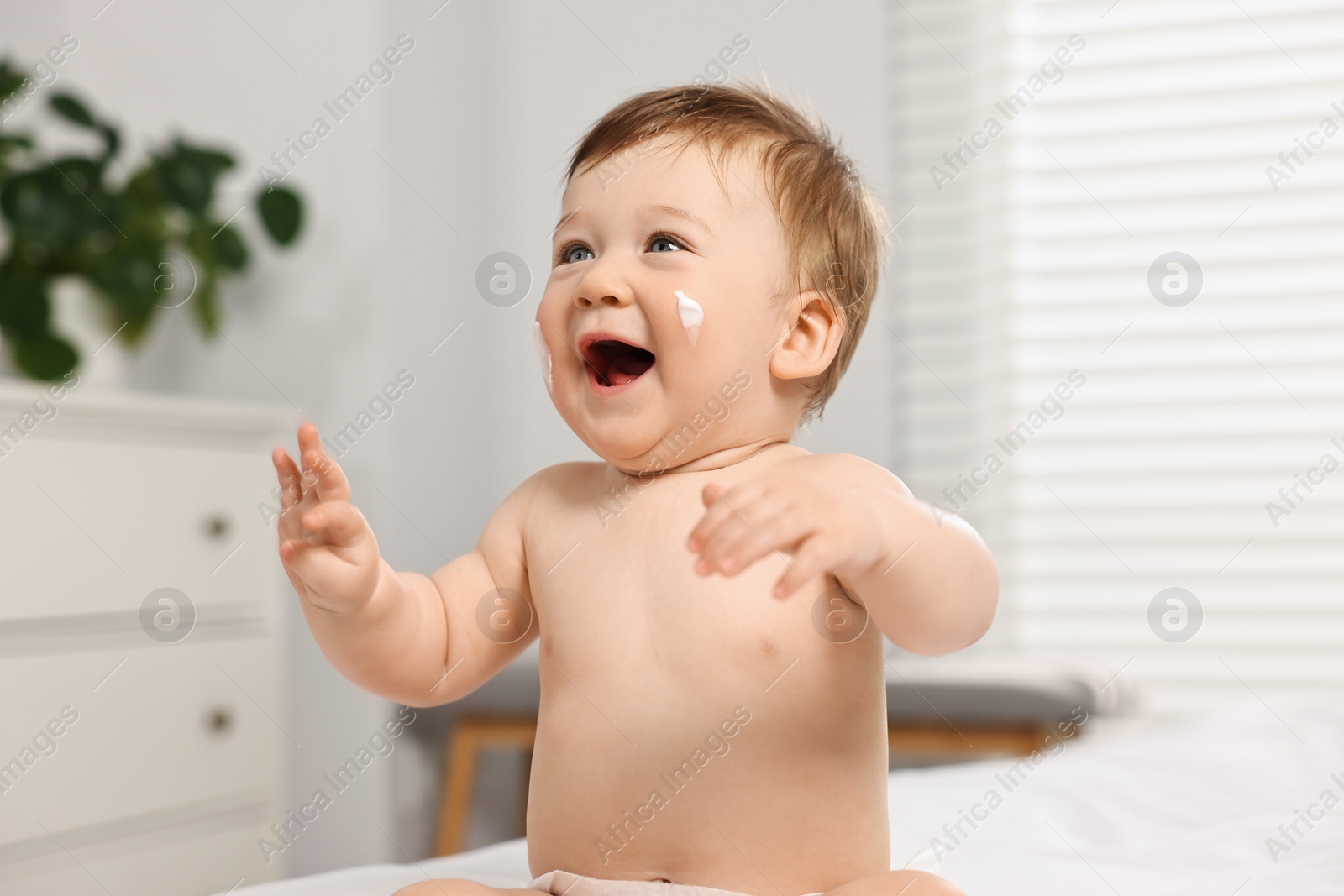 Photo of Cute little baby with moisturizing cream on face indoors