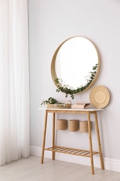 Photo of Round mirror and table with accessories near white wall. Modern interior design