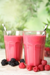 Photo of Tasty fresh milk shakes with berries on white wooden table against blurred background